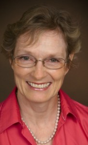 Smiling woman with glasses and pearl necklace.