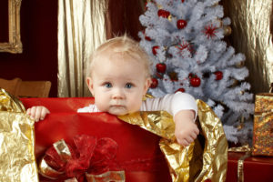 Baby looking out from a giftbox near a Christmas tree