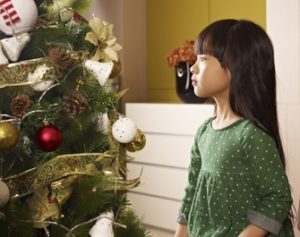 little asian girl sits next to christmas tree
