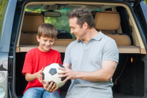 Father and son sit near car with opened boot and going to talk a