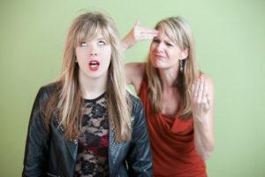 Frustrated mother behind angry daughter in provocative clothing