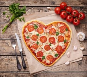 Heart shaped pizza margherita love concept for Valentines Day with mozzarella, tomatoes, parsley and garlic on vintage wooden table background.