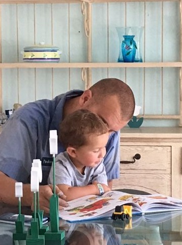 A man helps a young boy with reading at a kitchen table.