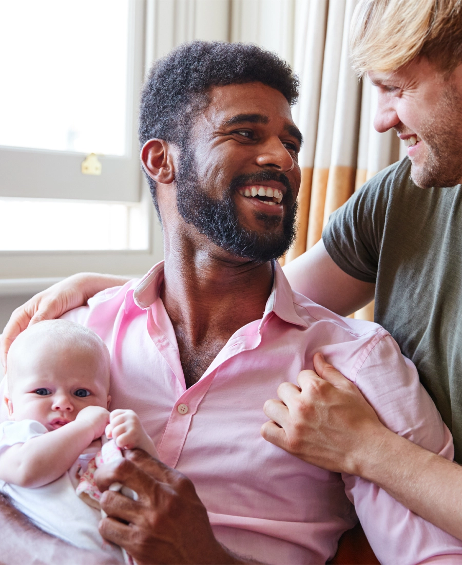 Two fathers smiling as they hold their baby at home