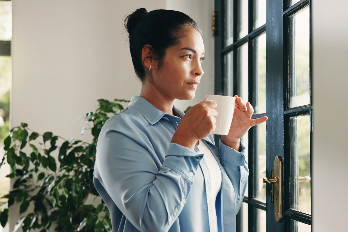 Woman holding a mug and looking thoughtfully out of a window